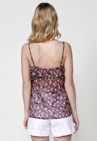 Top camicia floreale con spalline sottili, realizzato in tessuto nero trasparente, con un motivo di fiori rosa e bianchi. Dettaglio arricciato lungo lo scollo.
