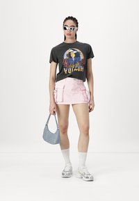 Tricou grafic gri cu design colorat, fustă cargo roz deschis, geantă albastră, ciorapi albi până la genunchi și adidași gri cu model.