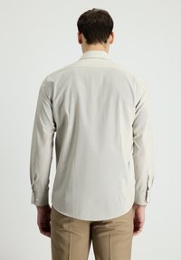 Camicia a maniche lunghe beige chiaro con colletto classico, texture liscia e polsini con bottone, che mostra sottili strisce verticali.