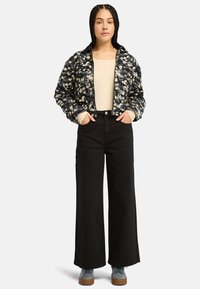 Giacca bomber trapuntata con stampa floreale, abbinata a pantaloni a gamba larga neri a vita alta. Colori navy, crema e denim con tessuto testurizzato.