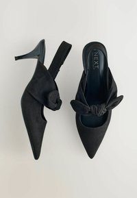 Chaussures à talons hauts en daim noir avec bout pointu et détail de nœud noué sur le dessus. Elles présentent un design à bride arrière et un talon brillant.