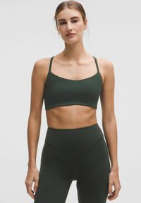 Sujetador deportivo de color verde oscuro con tirantes finos y una textura suave, combinado con leggings de cintura alta a juego que presentan un diseño sin costuras.