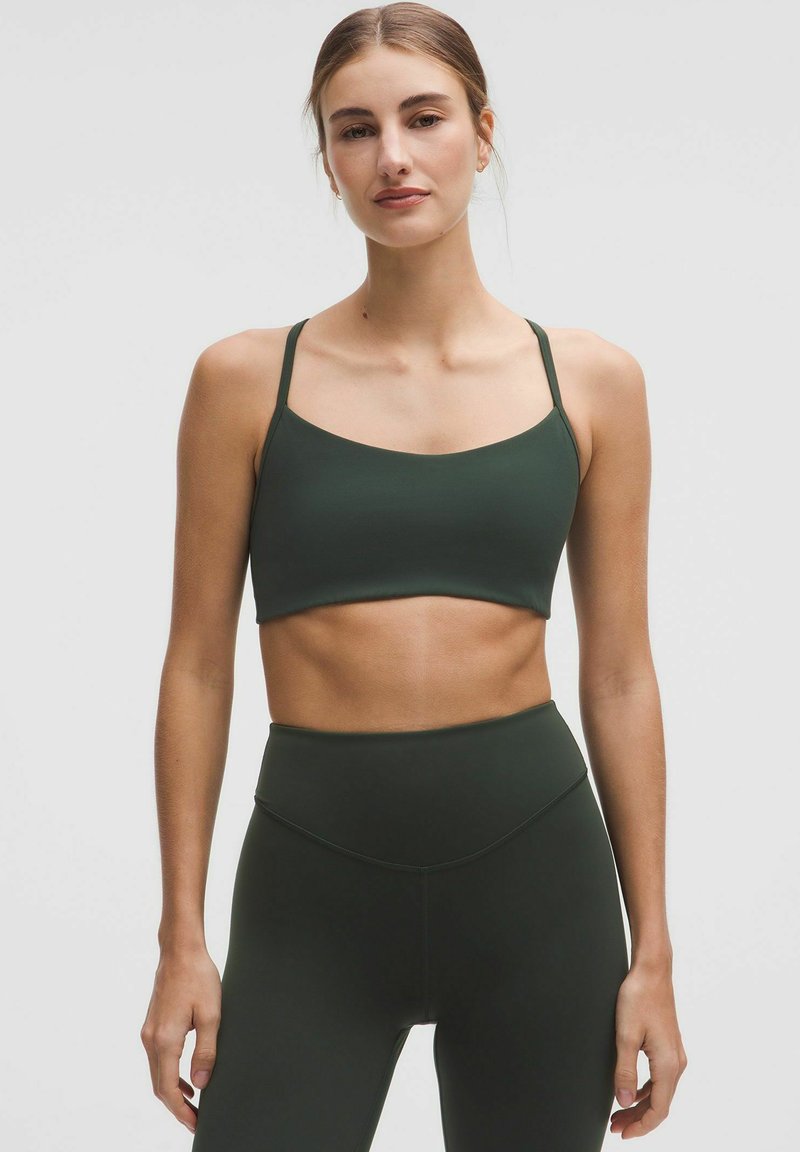 Sujetador deportivo de color verde oscuro con tirantes finos y una textura suave, combinado con leggings de cintura alta a juego que presentan un diseño sin costuras.