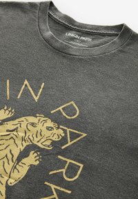 T-shirt en coton gris charbon avec un graphique de lion en or et le texte "LINKIN PARK". Col rond avec tissu texturé.