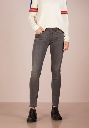 Jeans ajustados grises con una textura suave, diseño de cinco bolsillos y un ligero desgaste. Combinados con un suéter blanco con rayas rojas y azules.