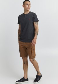 Kortermet mørkegrå henley-skjorte med tre knapper, kombinert med brune cargo shorts med side lommer, komplettert med svarte sneakers.