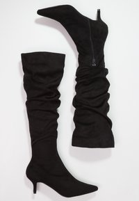 Botas negras hasta el muslo de suave ante con un diseño ligeramente caído, punta afilada, tacón de 7.5 cm y detalle de cremallera lateral.