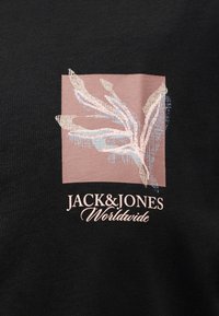 Αφηρημένο σχέδιο φύλλων σε μπεζ και ανοιχτό μπλε χρώμα πάνω σε τετράγωνο σκούρο ροζ, πάνω από το κείμενο "JACK & JONES Worldwide" σε μαύρο ύφασμα.