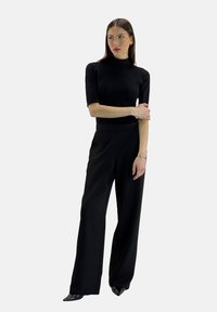 Sort tætsiddende rullekravebluse kombineret med højttaljede, vidbenede sorte bukser. Glat stof, lange ærmer og elegant design.