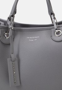 Szara skórzana torebka o fakturowanej powierzchni, srebrnym okućciu i zawieszce z logo. Posiada dwa uchwyty oraz oczka na górze.