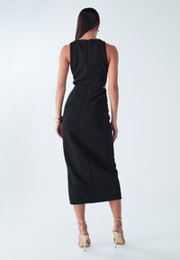 Must rihmavaba midi kleit kitsas siluetiga, peene selja tõmblukuga ja sileda, tekstuurse kangaga; kombineeritud rihmikute beežide kontsadega.