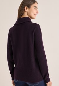 Gestrickter Pullover in tiefem Lila, mit hohem Kragen, langen Ärmeln und strukturiertem Stoff in lässigem Schnitt.