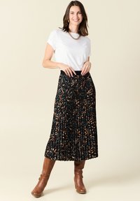 Zwarte geplooide rok met een bloemenpatroon in bruin en teal, gecombineerd met een witte t-shirt en bruine kniehoge laarzen. Fijne stofstructuur.