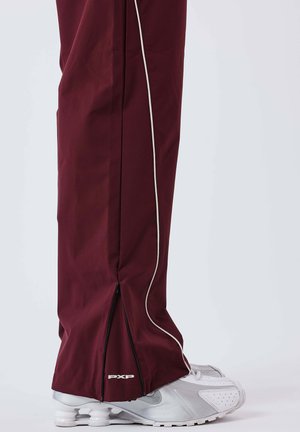 Maroon athletic pants with contrasting white side piping, zippered cuffs, and a "PXP" logo at the hem. Paired with silver sneakers.