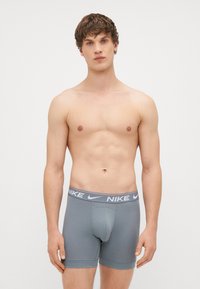 Pelēki kokvilnas bokseršorti ar Nike logo jostu, ar pieguļošu dizainu, gludu tekstūru un bez redzamām rakstāmzīmēm.