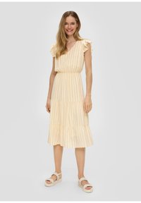 Hellgelbes Midi-Kleid mit V-Ausschnitt, vertikalen Streifen, Rüschensäumen und schichteltöen Rock. Kombiniert mit hellen Plateau-Sandalen.