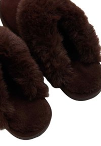 Pantuflas marrones con detalle de piel suave en la parte superior. Suela plana, forma redonda y material texturizado para mayor comodidad.
