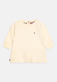 Sweatshirt couleur crème avec un motif texturé, col rond et manches longues raglan. Présente un petit logo et une fermeture à bouton à l'arrière.