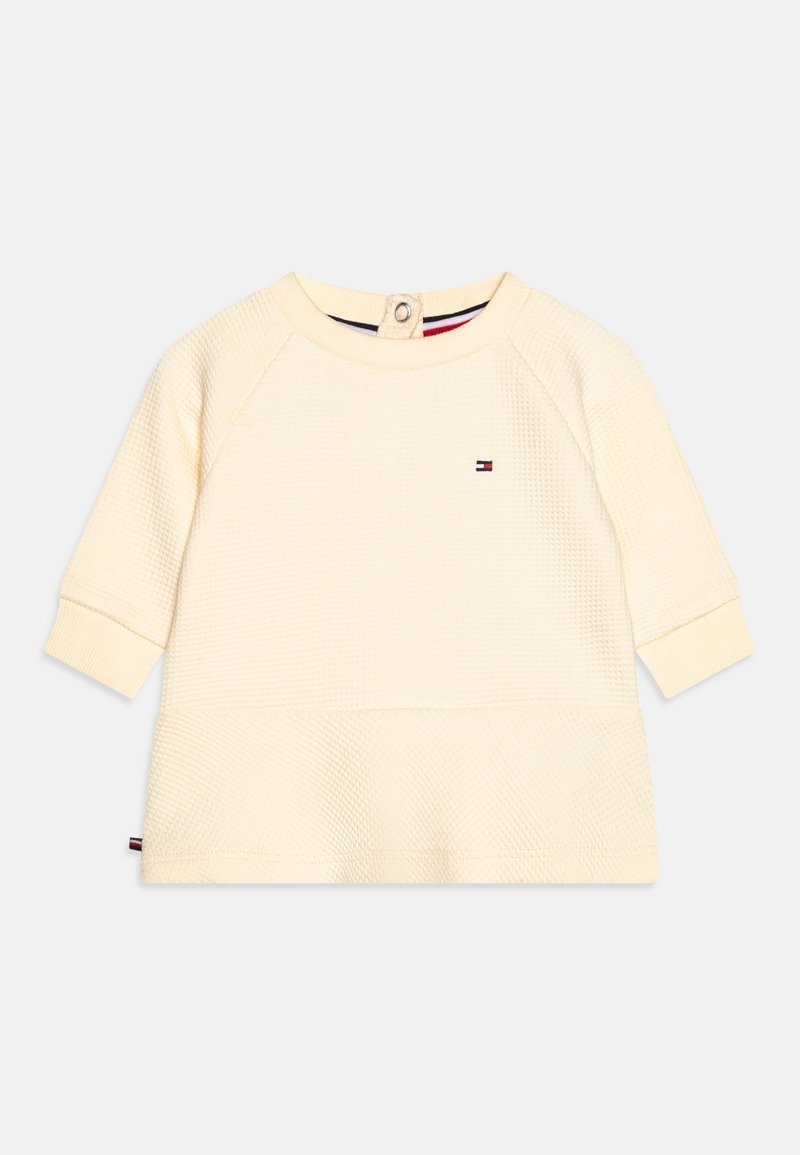 Sweatshirt couleur crème avec un motif texturé, col rond et manches longues raglan. Présente un petit logo et une fermeture à bouton à l'arrière.