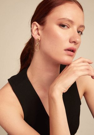 Pendientes de aro dorados con un Stud redondo y detalles entrelazados. El diseño presenta metal liso y un acabado pulido.