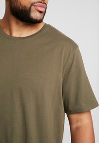 Olijfgroene t-shirt met korte mouwen en ronde hals, gemaakt van een zachte katoenmix; gladde textuur met een ontspannen pasvorm en schone stiksels.