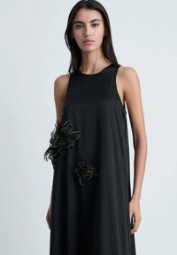 Black sleeveless dress in lightweight fabric with an A-line silhouette. Features intricate floral embroidery on the left side in black and metallic threads.