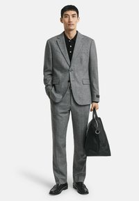 Grau Wolle Blazer und Hosenanzug mit einem schwarzen Poloshirt, kombiniert mit einer schwarzen Ledertasche mit strukturiertem Design und polierten Schuhen.