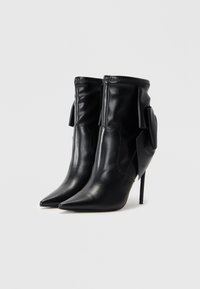 Bottines en cuir noir avec des pointes fines, un haut talon aiguille et un détail en tissu froncé au niveau de la cheville. Fermeture éclair à l'arrière.