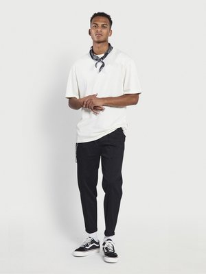 T-shirt blanche surdimensionnée, écharpe noire, pantalon noir fuselé et baskets noires avec semelles blanches. Design simple, sans motifs ni graphiques.