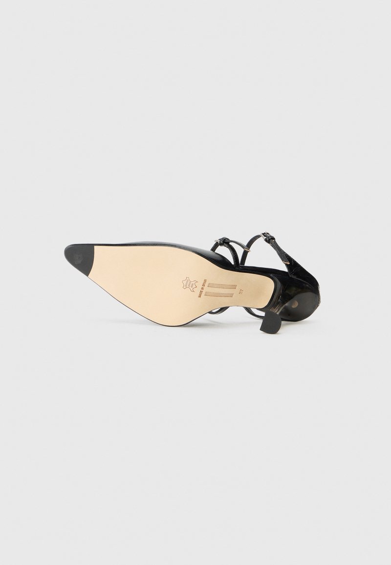 Black pointed toe shoe with glossy patent leather upper, thin ankle straps, and a light beige sole. Features a small heel.