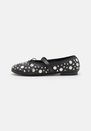 Zwarte platte schoen met zilveren ronde en kegelvormige studs, een klein strikje aan de voorkant en een enkele band over de bovenkant.