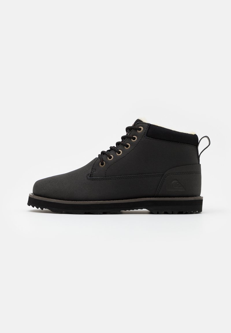Botines negros de tobillo fabricados con material impermeable, que presentan una superficie texturizada, punta redonda, diseño de cordones y una suela de goma con tracción.