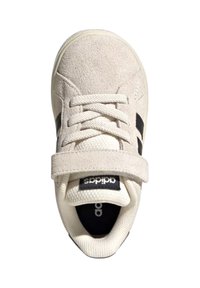 White suede sneaker with black accents, lace closure, Velcro strap, and textured tongue; features a round toe and cushioned interior.