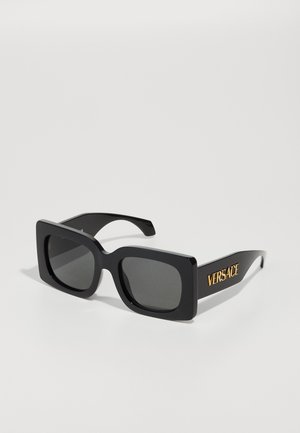 Óculos de sol retangulares pretos com armações de plástico espesso, lentes cinzentas e logótipo dourado "VERSACE" na lateral. Textura suave e brilhante.