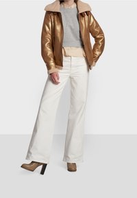 Gold metallic bomber jacket with shearling collar, gray sweater, layered striped top, white wide-leg pants, and brown heeled boots.