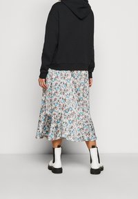 Svart luvtröja kombinerad med en midikjol i flera färger med blommönster i blått, vitt och brunt, samt svarta ankelstövlar med klack.