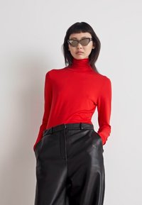 Röd långärmad polokrage topp kombinerad med svarta läderbyxor med hög midja, utformade med en slät yta och en åtsittande silhuett.