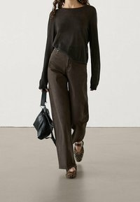 Bruna lösa byxor i kombination med en mörk långärmad topp, bärande en svart handväska, och iförd leopardmönstrade skor.