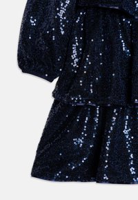 Robe bleu marine pailletée avec des paillettes regroupées, design à volants superposés et poignets élastiqués. Tissu doux avec une texture brillante.