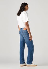 Blauwe denim jeans met een rechte pasvorm, voorzien van een leren patch op de achterkant van de taille en contrasterende stiksels. Combinatie met een eenvoudig wit t-shirt.