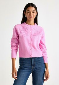 Lyserød cardigan med et struktureret bladdesign, rund halsudskæring og perleknapper. Ribbet manchetter og kant. Parret med mørkeblå jeans.