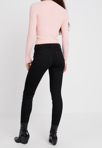 Růžový žebrovaný top s dlouhým rukávem ve spojení s úzkými černými džíny a lesklými černými kotníkovými botami na podpatku, pohled zezadu.