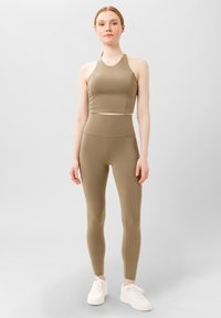 Khaki sportovní podprsenka a odpovídající legíny s vysokým pasem vyrobené z hladkého, elastického materiálu, doplněné bílými sportovními botami.