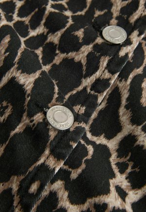 Leopardmönstrat tyg med beige fläckar på en mörk bakgrund, med synliga silverfärgade metallknappar, som visar ett texturerat och hållbart material.