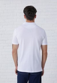 Hvid kortærmet polo-shirt med klassisk krave, glat tekstur og sideslidser, paired med mørk denimbukser.