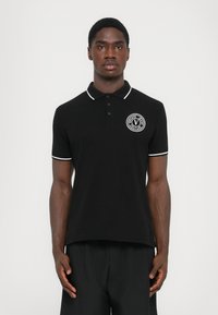 Cămașă polo neagră cu margine albă, având un logo circular la piept. Fabricată din material solid, cu guler clasic și mâneci scurte.