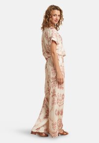 Lightweight, patterned jumpsuit in cream and pink hues with short sleeves, loose fit, and wide-leg pants, featuring a tied waist.