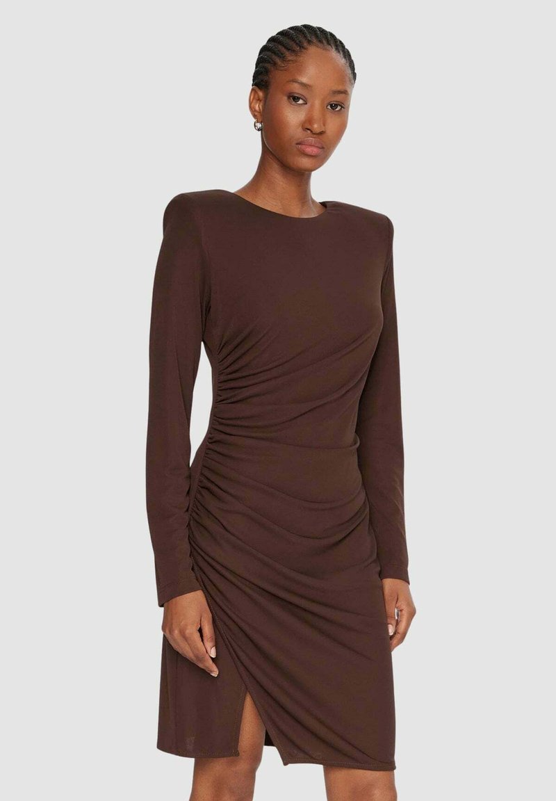 Vestito marrone a maniche lunghe con dettagli arricciati sul corpetto e spacco alto sulla coscia, realizzato in tessuto liscio. Semplice scollo rotondo.