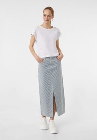 Biała bluzka krótki rękaw z haftowanymi detalami, zestawiona z długą, paskowaną spódnicą z rozcięciem z przodu, noszona z białymi sneakersami.