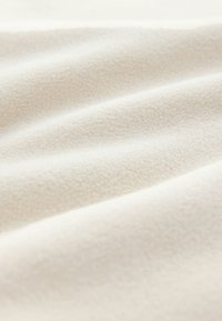 Weißer Fleece-Stoff mit weicher Textur und dezenten erhabenen Mustern, die sanfte Wellen und Falten über die Oberfläche zeigen.